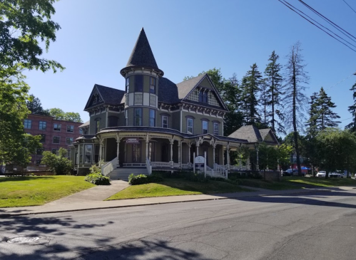 A large Victorian-style house with a turret, surrounded by trees and a well-maintained lawn on a sunny day.
