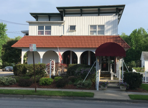 A two-story building with a red-tiled roof, white exterior, and a welcoming entrance under a maroon awning.