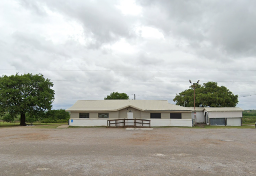 A single-story building with a light-colored exterior, surrounded by trees and a cloudy sky.