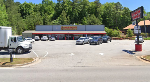 A parking lot with several cars in front of a store named "Parker Farms," surrounded by trees.