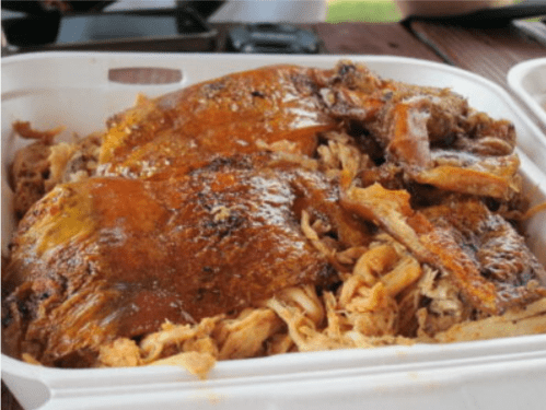 A close-up of a container filled with shredded and whole roasted chicken pieces, glistening with seasoning.