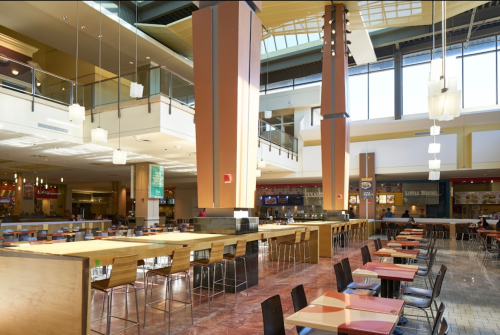 A spacious food court with tall ceilings, modern decor, and rows of tables and chairs, bustling with activity.