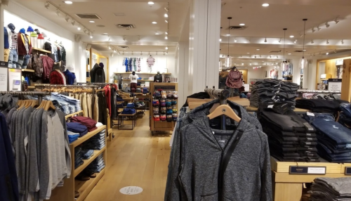 A clothing store interior with racks of apparel, including hoodies and jeans, and shelves of shoes in the background.