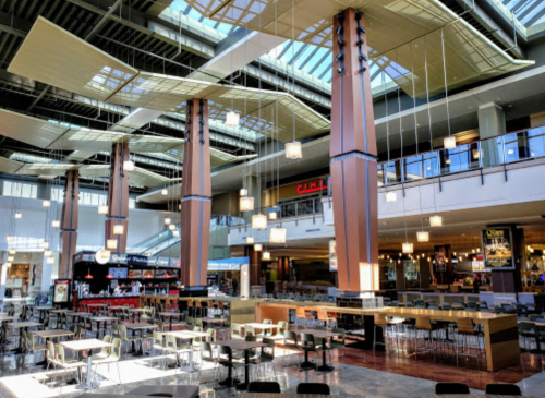 Bright, spacious food court with modern decor, large windows, and seating areas, featuring a cinema in the background.