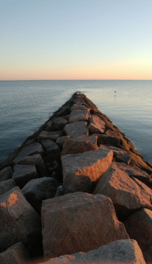 A rocky jetty extends into calm waters, with a soft sunset glow illuminating the scene.