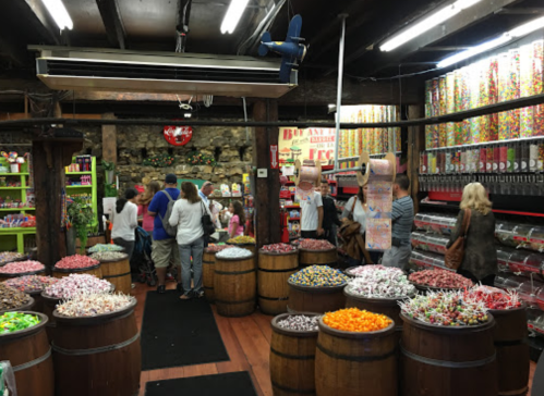 A colorful candy store filled with barrels of sweets and customers browsing the vibrant displays.