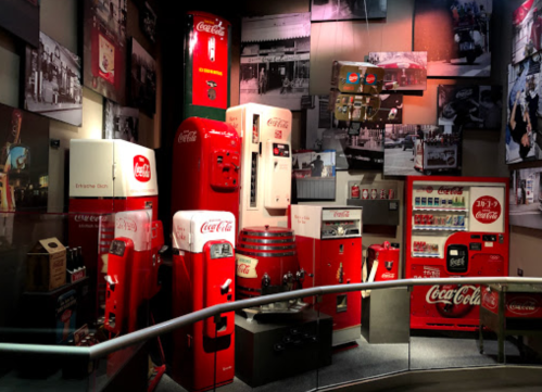 A display of vintage Coca-Cola vending machines and memorabilia in a museum setting.