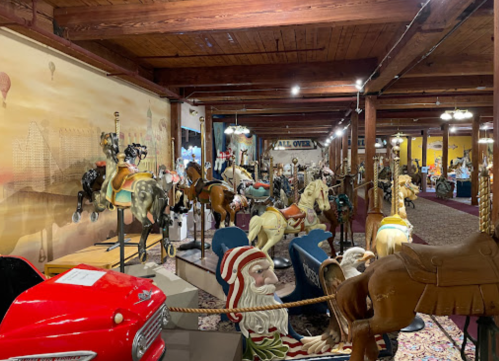 A vintage carousel exhibit featuring intricately carved horses and other rides in a warmly lit museum space.