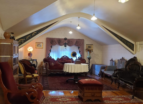 A cozy attic room with vintage furniture, a round table, and decorative accents under a sloped ceiling.