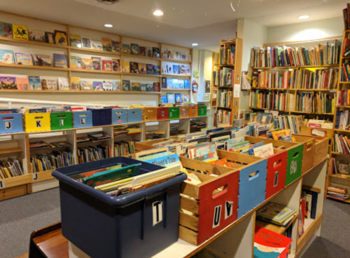 A cozy library with shelves of books and colorful bins filled with children's books.
