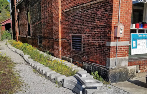 A brick building with a flower garden and a gravel path lined with stone blocks.