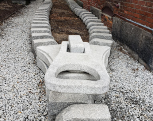 A curved arrangement of large stone blocks resembling a zipper on a gravel surface near a brick wall.