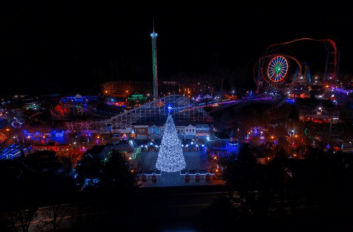 A vibrant amusement park illuminated with colorful lights, featuring a large Christmas tree and festive attractions at night.