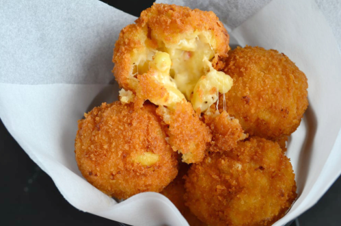 A basket of golden, crispy fried balls with melted cheese oozing from one, showcasing a delicious, gooey interior.