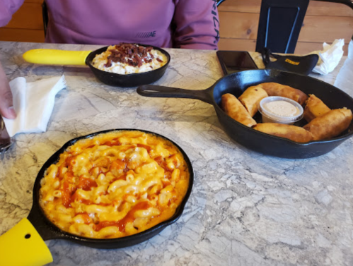 A table with two cast iron dishes: one with macaroni and cheese, the other with spring rolls and dipping sauce.