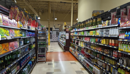 A grocery store aisle filled with various beverages, including sodas, juices, and sparkling water on both sides.