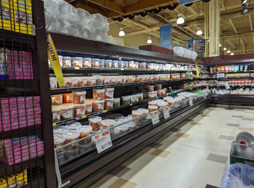 A grocery store aisle filled with various containers of food, including soups and salads, on shelves.