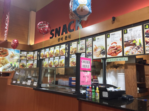 A snack shop interior featuring a menu board with various food items and colorful balloons.