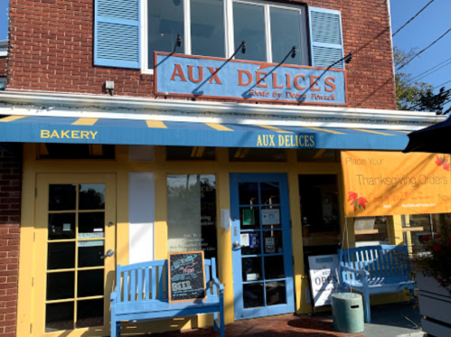 A bakery storefront with blue shutters, yellow awning, and a sign for Thanksgiving orders. Two blue benches outside.