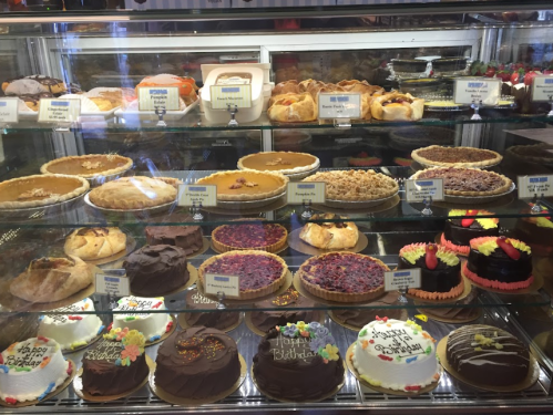 A display case filled with various pies, cakes, and pastries, each labeled with names and messages.
