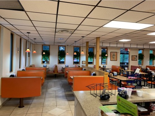 Interior of a casual dining restaurant with orange booths, tables, and hanging plants, featuring a counter in the foreground.