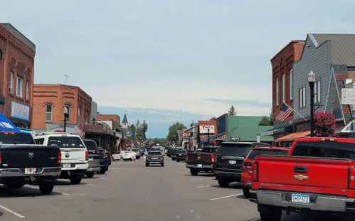 A view of a small town street lined with shops and parked trucks under a clear sky.