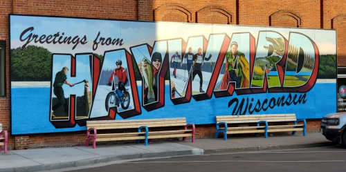 Mural greeting from Hayward, Wisconsin, featuring outdoor activities and vibrant colors on a brick wall.