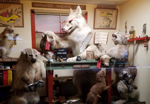 A whimsical display featuring a wolf judge presiding over stuffed animals in a courtroom setting.
