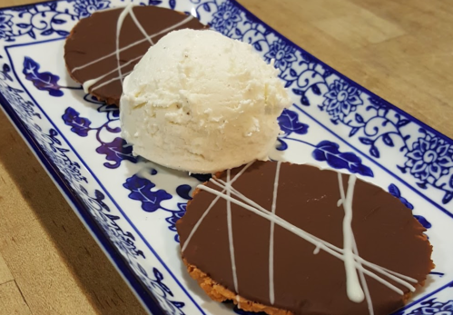 A decorative plate holds two chocolate-covered cookies and a scoop of vanilla ice cream.