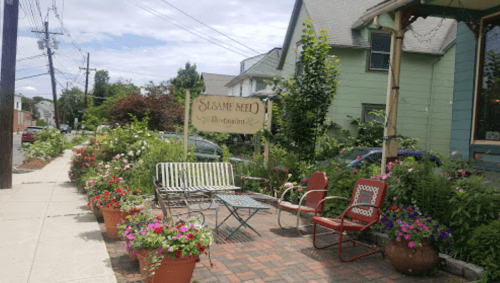 A charming restaurant entrance with colorful flowers, outdoor seating, and a sign for "Sesame Seed Restaurant."