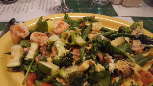A colorful plate of mixed vegetables, shrimp, and pasta, garnished with cheese and served on a yellow dish.