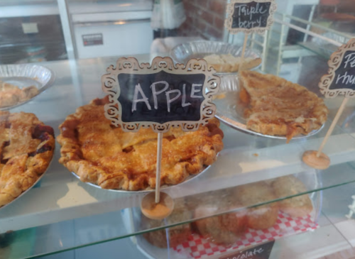 A display case with various pies, including a labeled apple pie, showcasing their golden crusts and fillings.