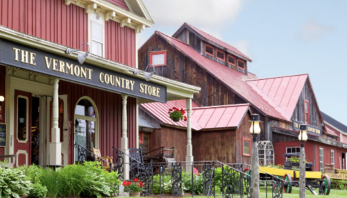 A charming red building with a sign reading "The Vermont Country Store," surrounded by greenery and rustic architecture.