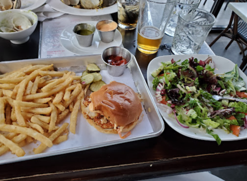 A tray with fries, a sandwich, and a side salad, accompanied by drinks and condiments on a table.
