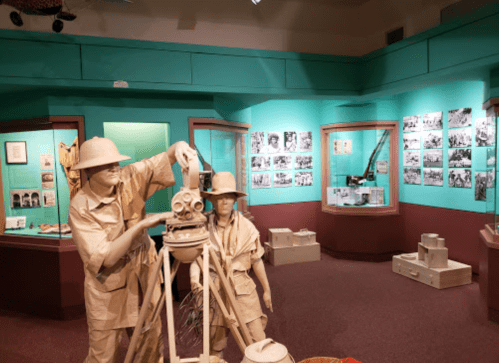 A museum exhibit featuring life-sized figures of surveyors with equipment, surrounded by historical photographs and artifacts.
