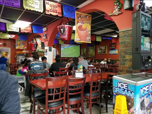A lively restaurant interior with patrons watching a soccer game on a large screen, colorful decorations overhead.
