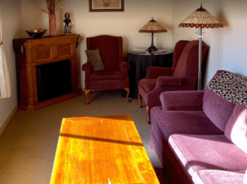 Cozy living room with two armchairs, a sofa, a wooden coffee table, and lamps, featuring warm lighting and a fireplace.