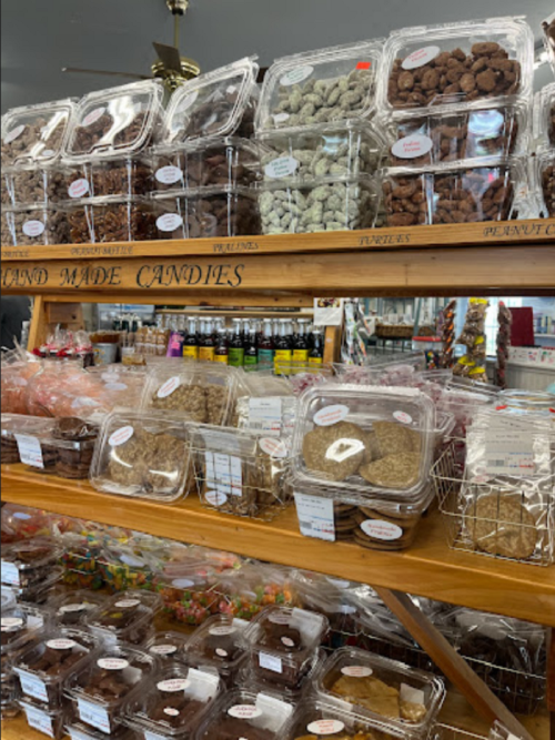 A display of various homemade candies and treats in clear containers on wooden shelves.