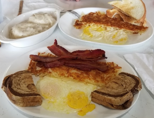 Two plates of breakfast: one with eggs, bacon, hash browns, and toast; the other with biscuits and gravy.