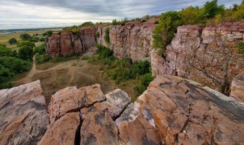 A rocky cliff with greenery, overlooking a valley under a cloudy sky.