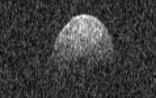 A grainy, monochrome image of a celestial object, possibly an asteroid, with a rounded shape against a dark background.