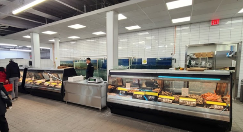 A clean grocery store meat section with display cases filled with various meats and a staff member serving customers.