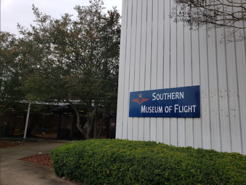 Sign for the Southern Museum of Flight, with trees and a building in the background.