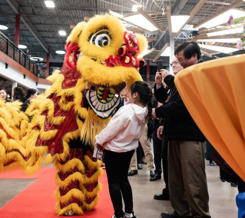 A vibrant lion dance performer interacts with a young girl at a festive event, surrounded by onlookers.