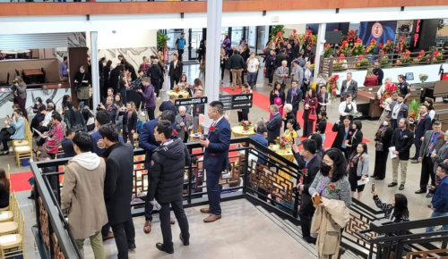 A crowded event space with people mingling, decorated with flowers and banners, viewed from an upper level.