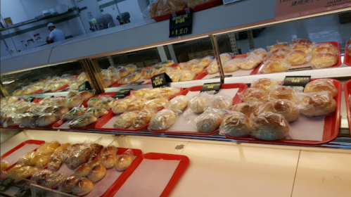 A display of various baked goods in plastic packaging on red trays in a bakery.