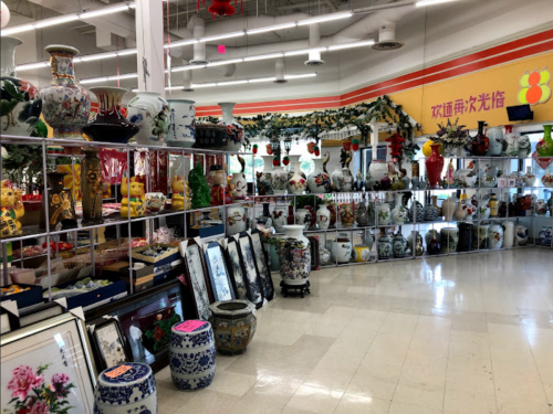 A brightly lit store aisle filled with decorative vases, pottery, and framed art on display.