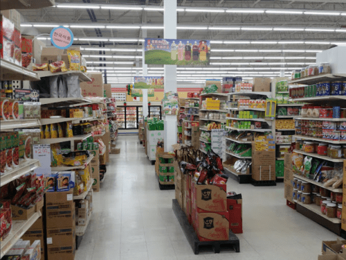A grocery store aisle filled with various food products on shelves and displays, with bright lighting overhead.