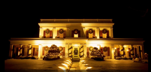 A beautifully lit house at night, adorned with wreaths and surrounded by snow-covered landscaping.