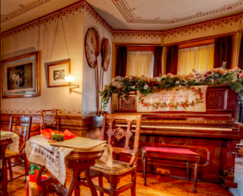 Cozy vintage dining room with a decorated piano, festive table settings, and warm lighting.